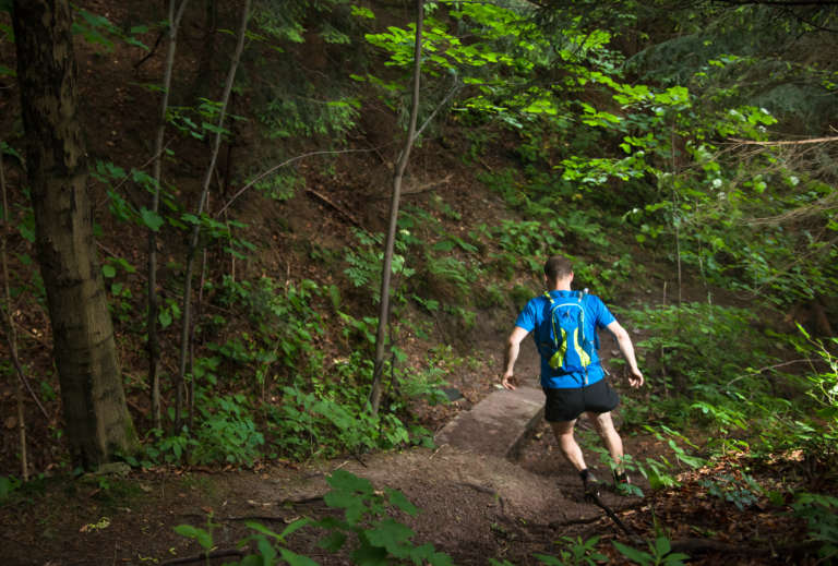 man with bag running on the trail down the steep hill in the green forest